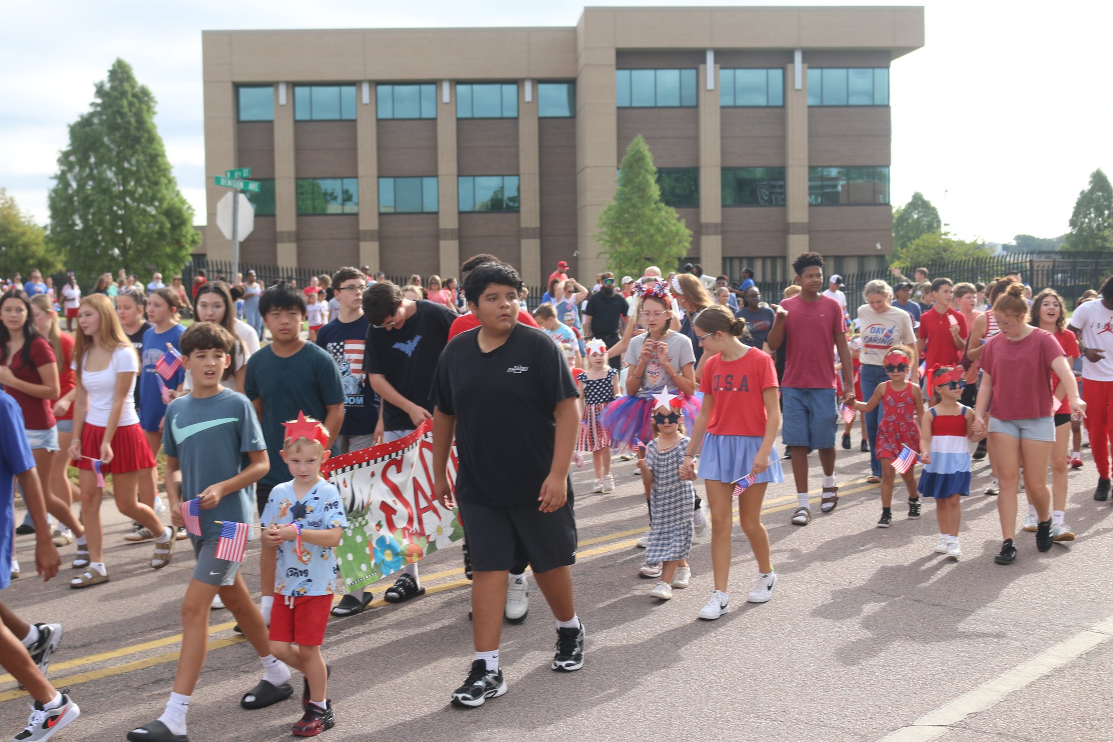 Large crowd marching with Sadler Arts Academy banner visible in the Patriotic Parade